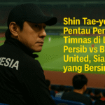 Shin Tae-yong duduk di tribun stadion sambil memantau pertandingan Persib vs Bali United dengan serius, mengenakan jaket bertuliskan INDONESIA